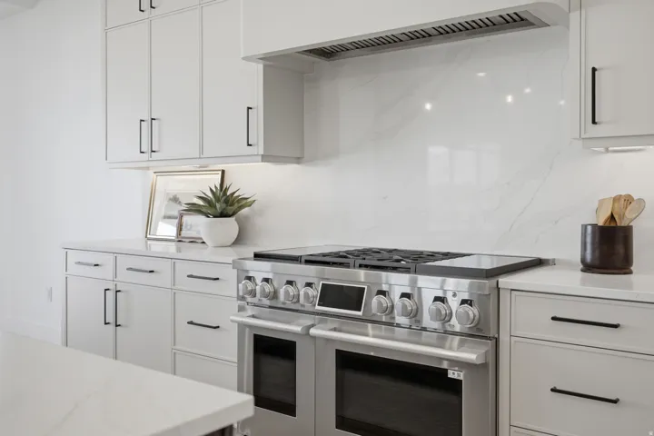 Stainless steel range with a built-in hood, quartz countertops, white cabinetry with black hardware, and a matching full-height backsplash