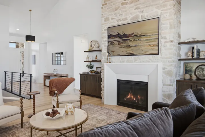 Stone-clad fireplace with a white mantel, light wood-finish flooring, vaulted ceiling, and built-in shelving