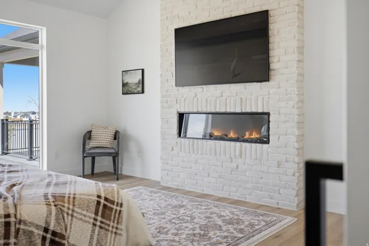 Vaulted ceiling with an integrated linear fireplace, light wood-finish flooring, and a glass-paneled door opening to a balcony with black metal railings
