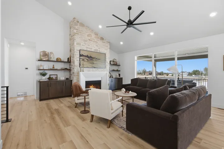 Vaulted ceiling with recessed lighting, stone-clad fireplace with mantel, built-in shelving, wood-finish flooring, and expansive sliding glass doors