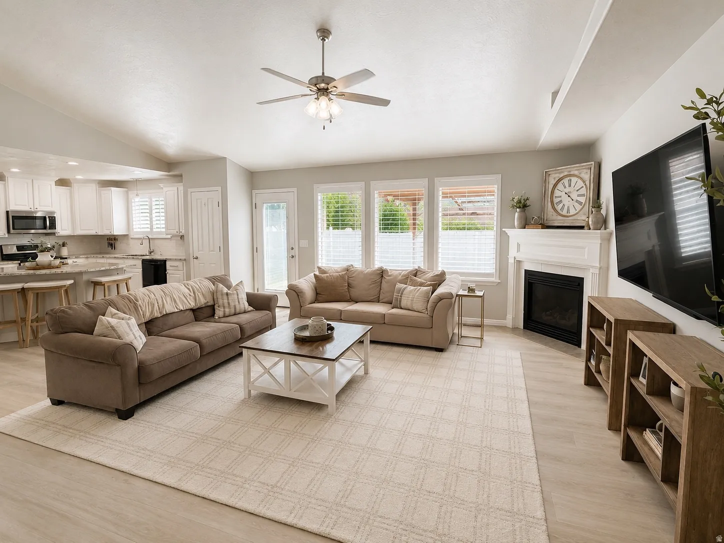 Vaulted ceiling with a ceiling fan, fireplace with a white mantel, three windows with blinds, and light wood-finish flooring