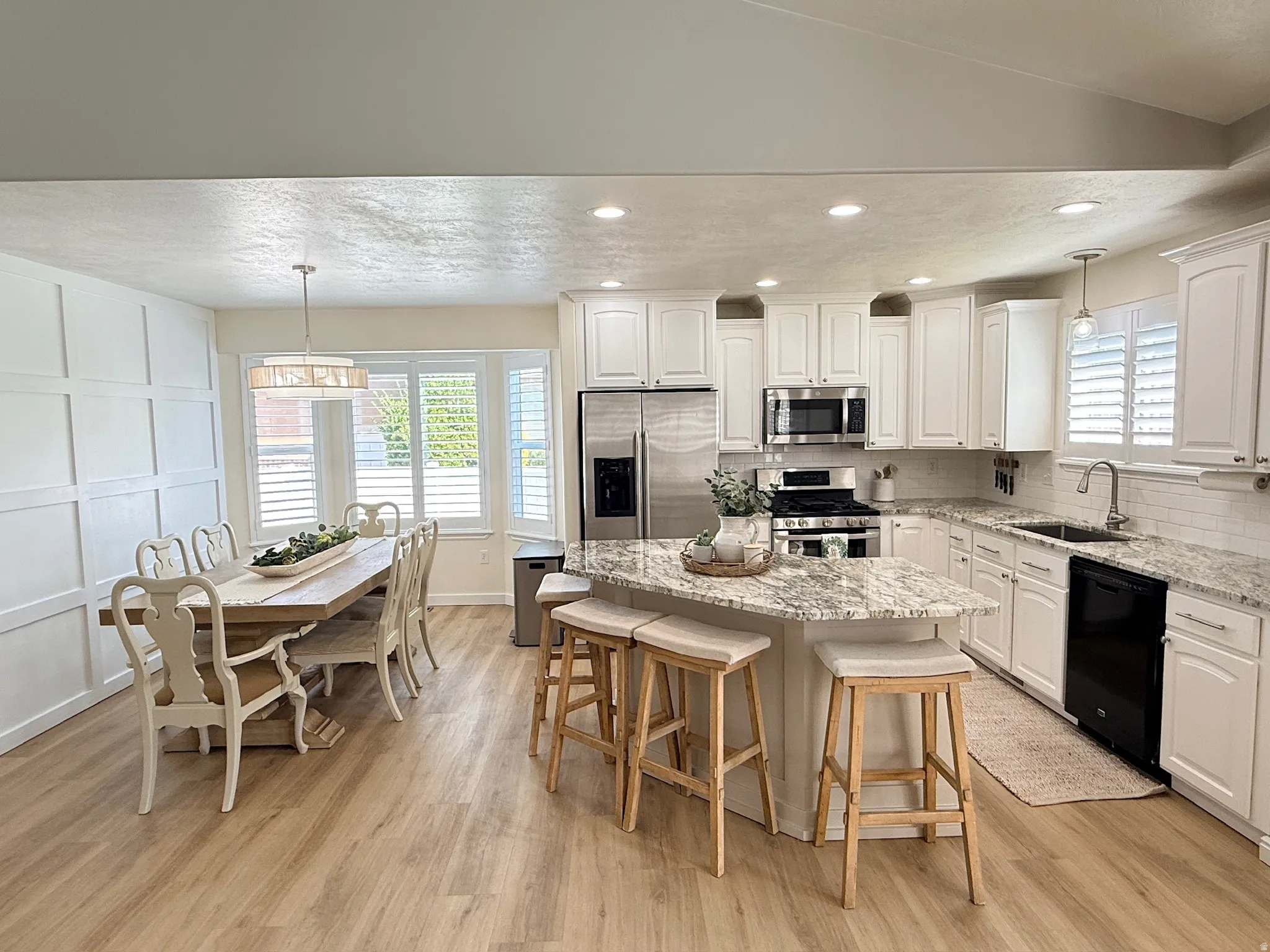 White shaker cabinetry, stainless steel appliances, granite countertops, wood-finish flooring, and a decorative board and batten wall