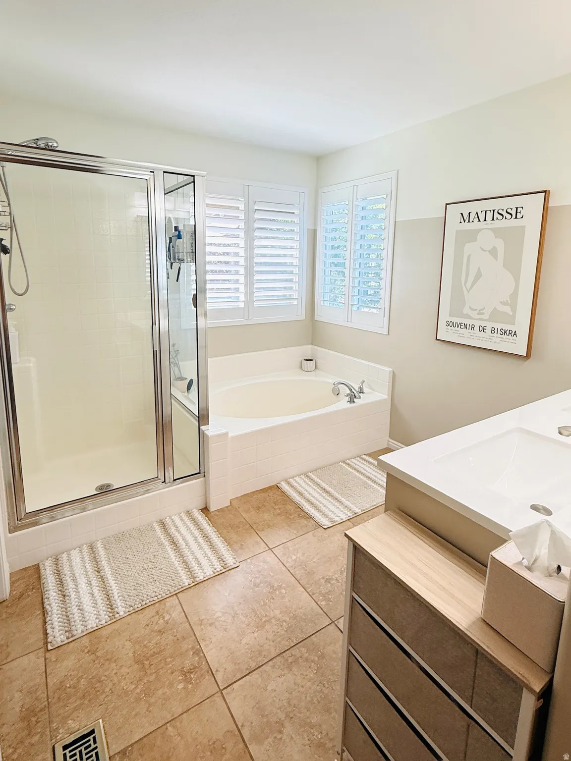 Corner soaking tub with tile surround, walk-in shower with glass enclosure, white plantation shutters, and a vanity with an integrated sink