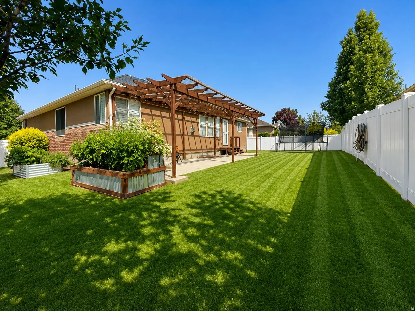 Expansive lawn with a white privacy fence, concrete patio, and pergola