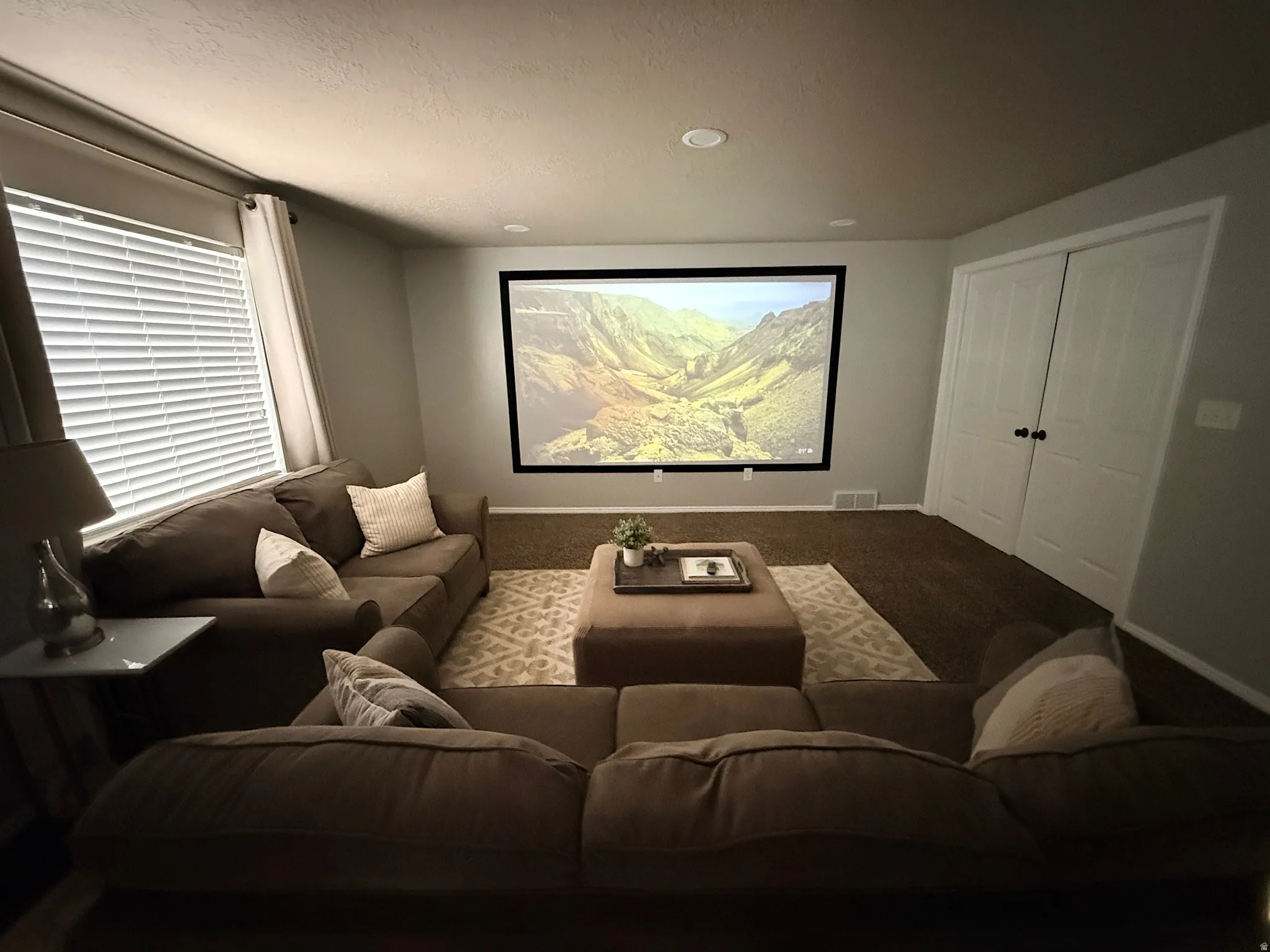 Projector screen with recessed lighting, light-colored walls, and a window with blinds