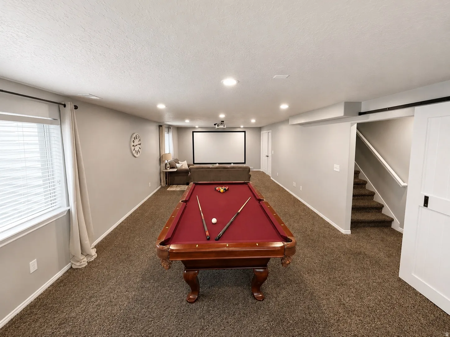 Spacious lower level featuring plush carpeting, recessed lighting, a built-in projection screen, and a sliding barn door