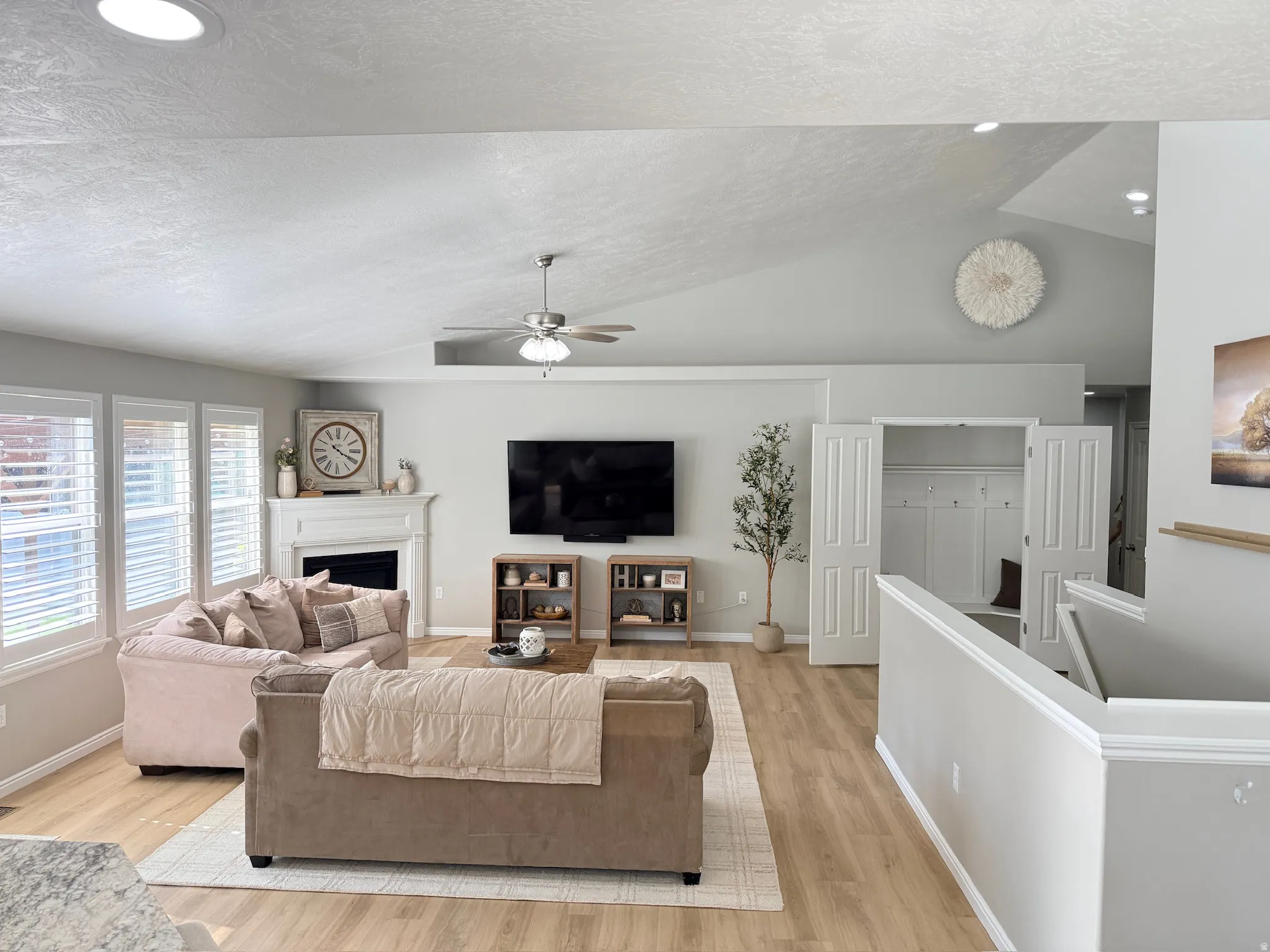 Vaulted ceiling with recessed lighting, wood-finish flooring, fireplace with mantel, white window shutters, and built-in closet storage
