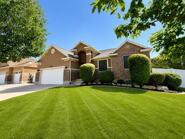 Stucco and brick exterior with a pitched roof, two-car garage, and landscaped front yard with shrubs and a rock border