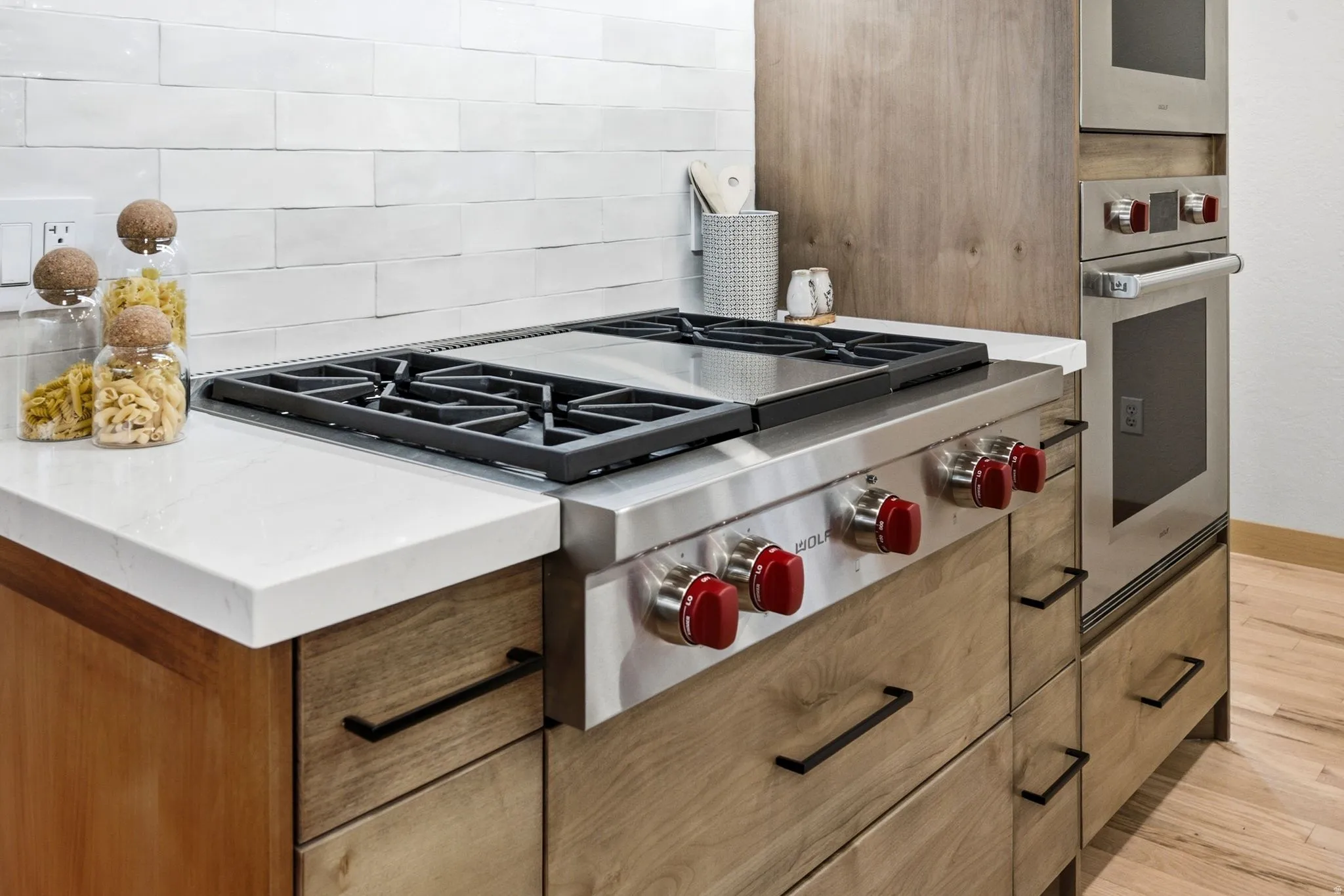 Stainless steel Wolf gas range with, 2 built-in stainless steel Wolf ovens (Convection/conventional and steam), quartz countertop, and high-end natural wood cabinetry.