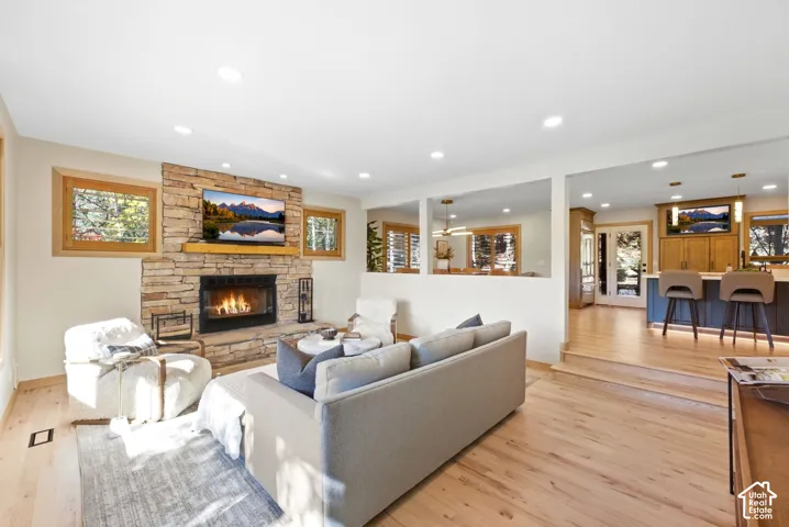 Stone-clad fireplace with a wood mantel, light wood-finish flooring, recessed lighting, and a partial wall separating living spaces