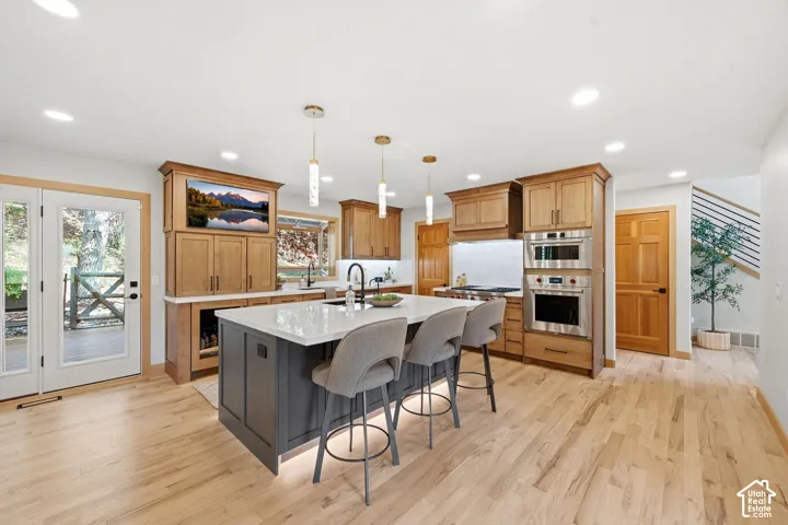Kitchen featuring a center island with under-cabinet lighting, stainless steel double Wolf ovens (convection and steam), high-end wood-finish cabinetry, and light refinished wood flooring