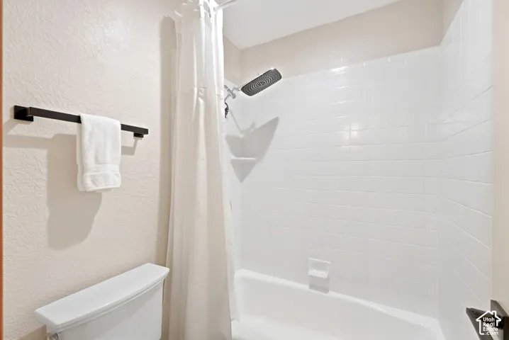 Bathtub and shower combination with white subway tile surround, a dark finish shower head, and a white toilet