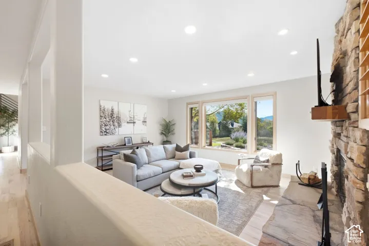 Recessed lighting, wood-finish flooring, stone-clad fireplace, large picture windows, and light neutral wall tones
