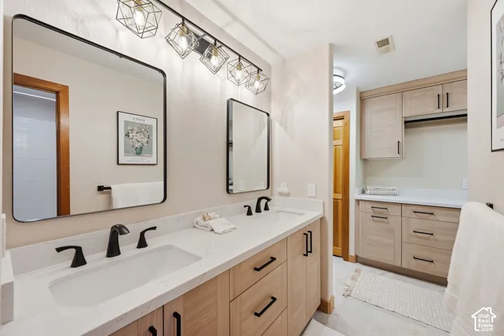 Dual vanity with integrated sinks and matte black fixtures with Valor Gold Lava quartzite countertops, heated floors, and updated lighting.