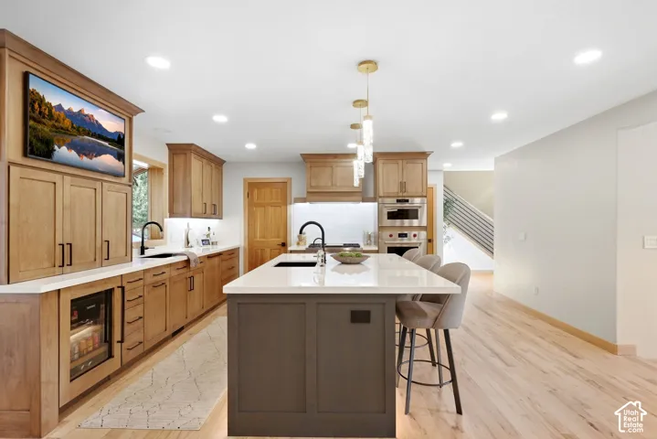 Kitchen featuring an expansive island with seating, integrated stainless steel appliances, light wood-finish cabinetry, recessed ceiling lighting, and wood-finish flooring