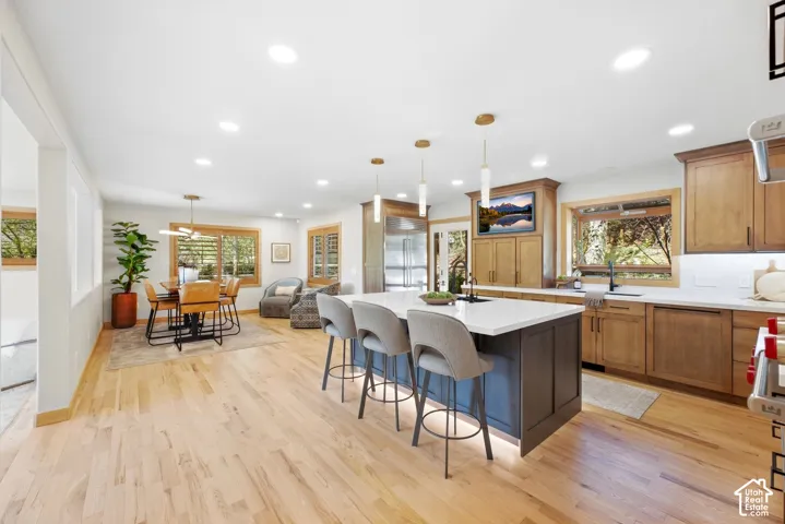 Kitchen with natural wood-finish flooring, white countertops, a dark-toned island with integrated lighting, and recessed ceiling lights