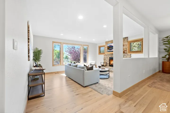 Recessed lighting, wood-finish flooring, stone-clad fireplace with wood mantel, large windows with wood trim, and a partial wall with decorative cutouts