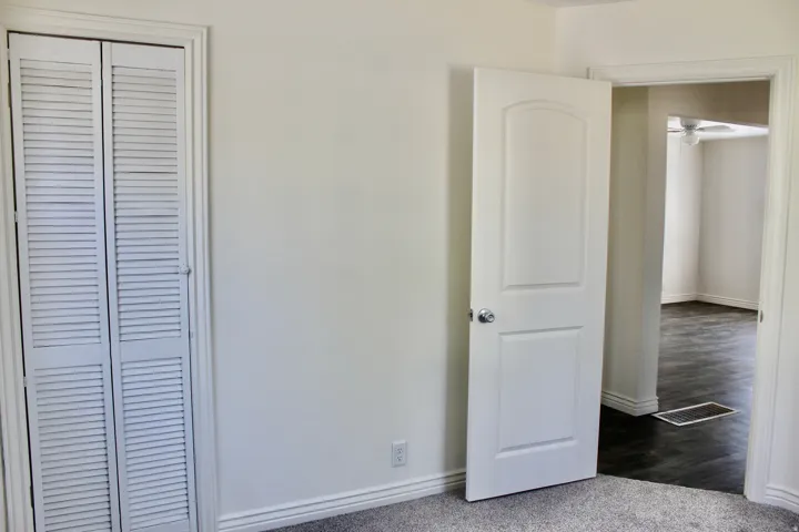 Bright bedroom suite featuring neutral walls, louvered closet doors with storage capacity, an open walk-in closet area with hanging rod, and polished concrete flooring throughout