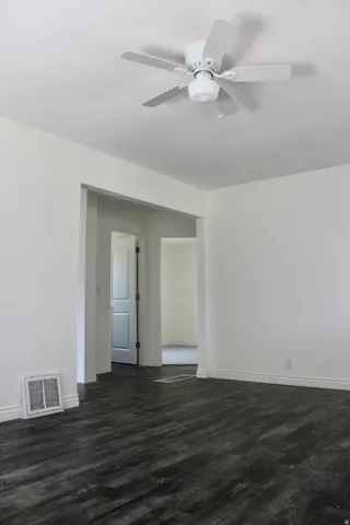Dark wood-finish flooring, white walls, ceiling fan, and white trim throughout