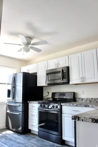 White cabinetry, stone-finish countertops, stainless steel appliances, and wood-finish flooring