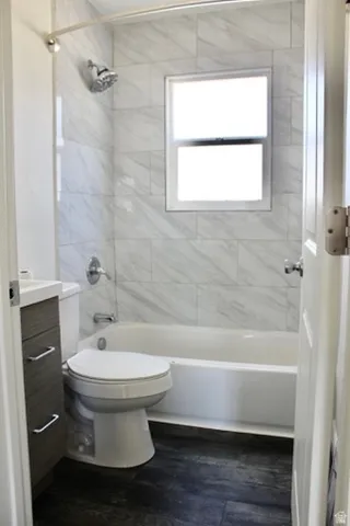 Shower/bathtub combination with a curved shower rod, contemporary vanity with a white countertop and chrome hardware, white toilet, and wood-finish flooring