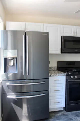Stainless steel refrigerator, white shaker-style cabinetry, granite-style countertops, black oven range, and black built-in microwave