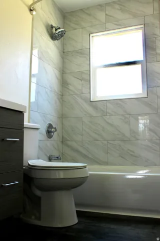 Bathtub with white tile surround, a single window, and a rain showerhead