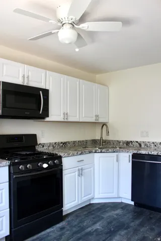 White cabinetry, dark wood-finish flooring, stainless steel faucet, built-in microwave, and black range