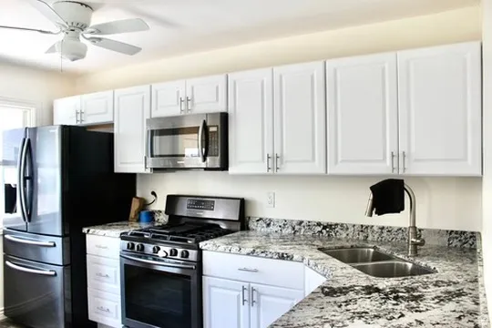 Kitchen featuring white shaker-style cabinetry, a double basin stainless steel sink, stainless steel appliances, and a ceiling fan with integrated lighting