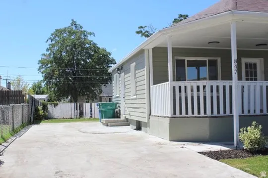 Siding exterior with a covered porch, white porch railing, concrete driveway, and an established tree