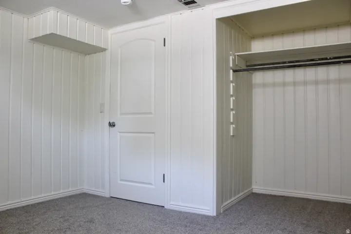White paneled walls, gray carpet flooring, white interior door, and built-in closet with shelving and hanging rod