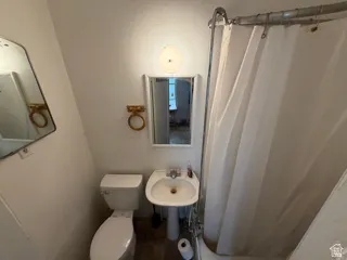 Unit 2 bathroom. Pedestal sink with mirror and wall-mounted light fixture, adjacent to a toilet and shower with a curtain rod
