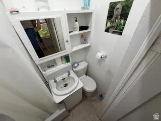 Unit 1 bathroom. Pedestal sink with dual faucets, built-in medicine cabinet with mirrored door, wall-mounted shelving, and toilet with a white tank
