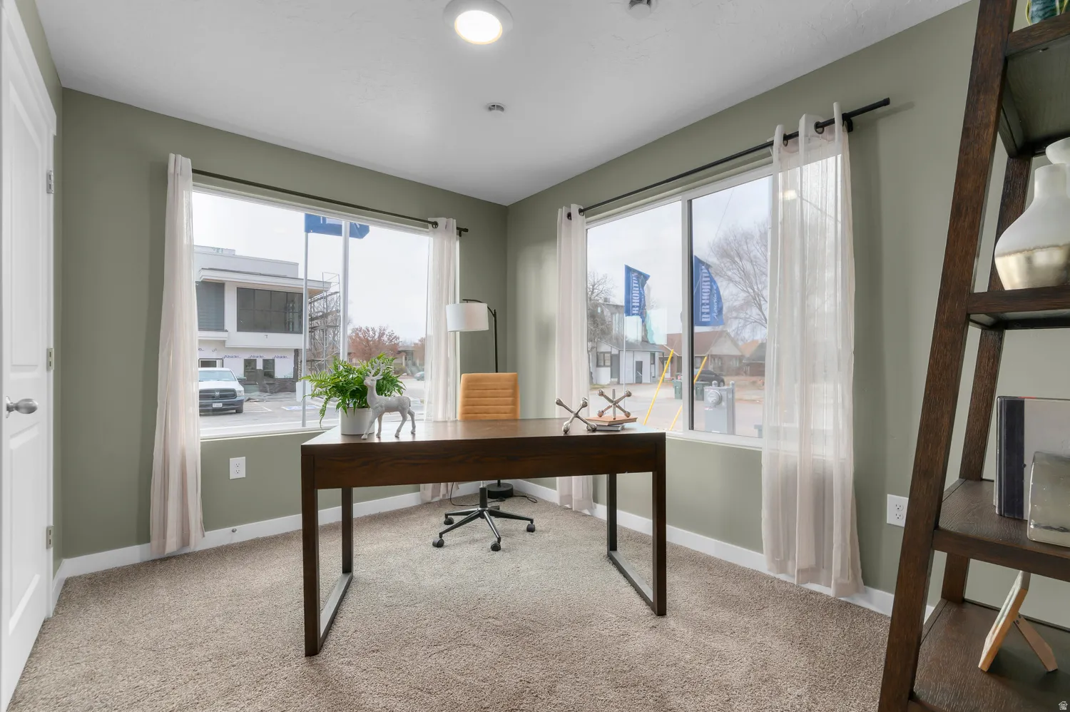 Recessed lighting and two large windows illuminate this room with light green walls and carpet flooring