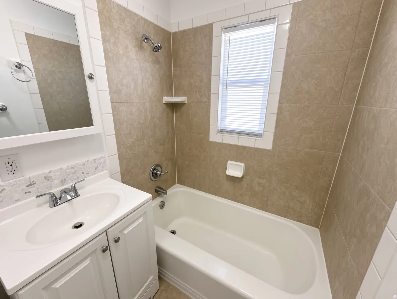 Updated bathroom featuring ceramic tile walls, white cabinetry with integrated sink, chrome fixtures, and an alcove bathtub with shower combination
