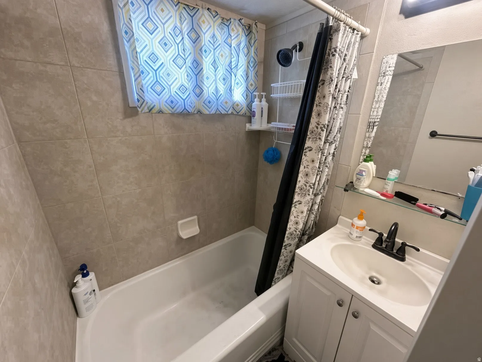 White bathtub with tiled surround, single vanity with integrated sink, and wall-mounted mirror