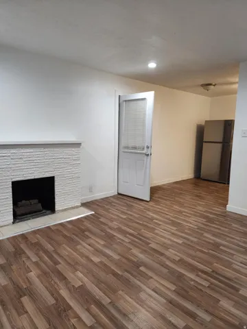 Wood-finish flooring throughout, featuring a white brick fireplace with a tiled hearth