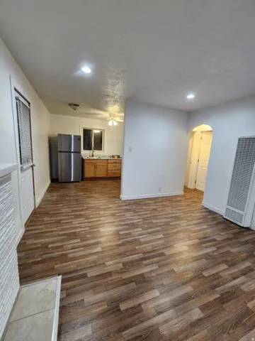 Wood-finish flooring throughout, recessed lighting, and a kitchen featuring wood cabinetry and a stainless steel refrigerator