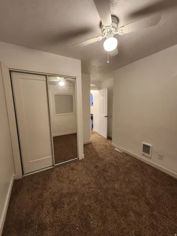 Sliding closet doors with mirrored panel, ceiling fan with integrated lighting, wall-mounted heating unit, and brown carpeting