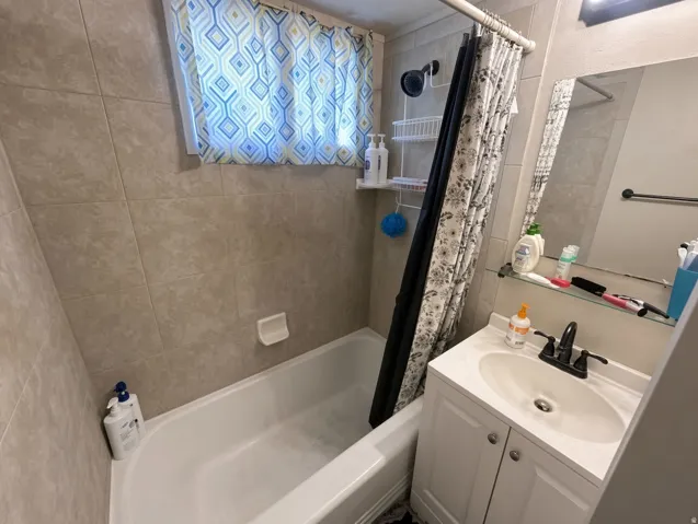 White bathtub with tiled surround, single vanity with integrated sink, and wall-mounted mirror