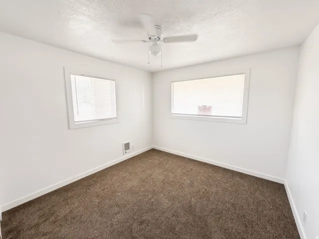 Neutral wall finishes, textured carpeting, two distinct windows, and a ceiling fan