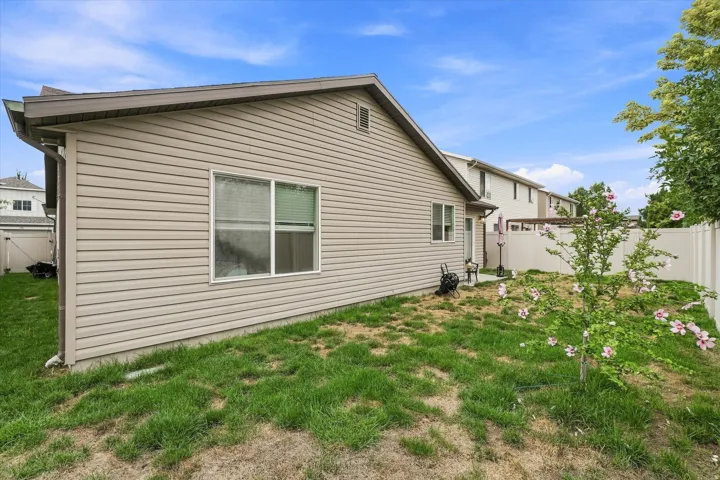 Spacious backyard featuring a manicured lawn with mature landscaping and newly planted shrubs, enclosed by a vinyl privacy fence