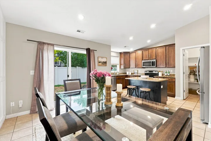 Open-concept kitchen and dining area featuring wood-finish cabinetry, stainless steel appliances, tile flooring, and a center island with seating