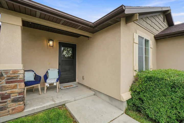 Welcoming covered entry featuring a black paneled door with wreath accent, stacked stone accent wall, warm exterior lighting, and concrete patio