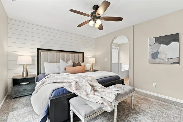 Primary Bedroom with Shiplap Accent Wall, Ceiling Fan with Integrated Lighting, Arched Doorway Entry, Hardwood-Finish Flooring, and Coordinating Nightstands with Task Lighting
