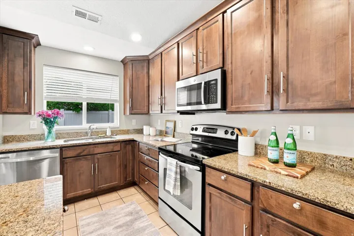 Kitchen featuring wood cabinetry, stainless steel appliances, speckled countertops, and tile flooring