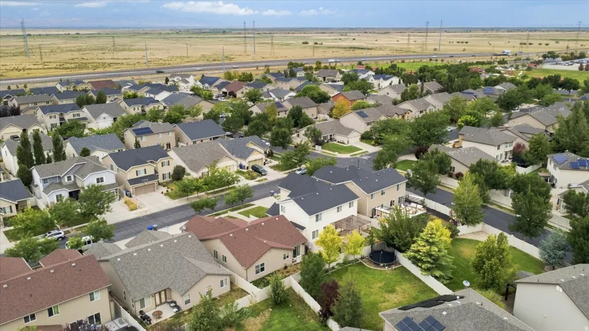 Aerial view of an established residential neighborhood featuring single-family homes with varied architectural styles, mature landscaping throughout the community, and expansive open plains visible beyond the developed area