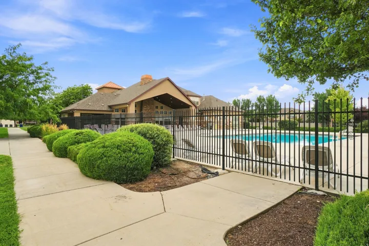 Outdoor swimming pool with a surrounding wrought iron fence, concrete decking, and adjacent building with covered patio