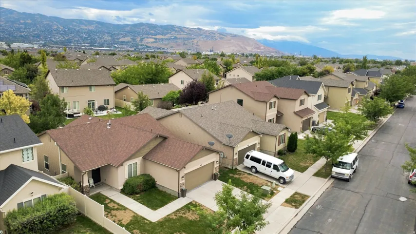 Aerial view showcasing a multi-level residence with a two-car garage, composite roofing, and a manicured front landscape