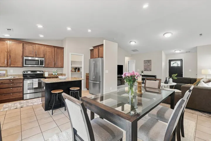 Open-concept living space featuring a chef's kitchen with wood-finish cabinetry, stainless steel appliances, and a black island with seating, flowing into a dining area with a glass-top table and into a comfortable living room with built-in seating